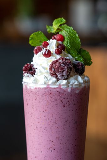 A vertical shot of a berry milkshake served with whipped cream on top in a blur