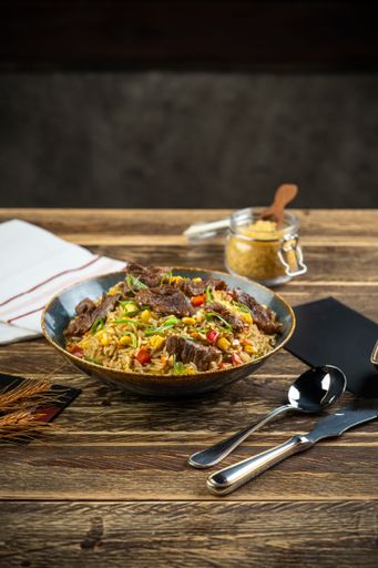 A Fried rice dish with beef pieces and cutlery on a wooden table, vertical shot