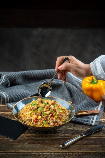 A male hand scooping a spoon from a Fried rice dish on a wooden table, vertical shot