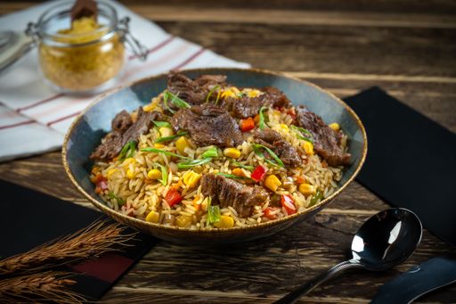 A Fried rice dish with beef pieces and cutlery on a wooden table