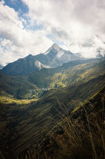 A vertical shot of a Mountain Austrian alps with green grass and snow and under cloudy sky