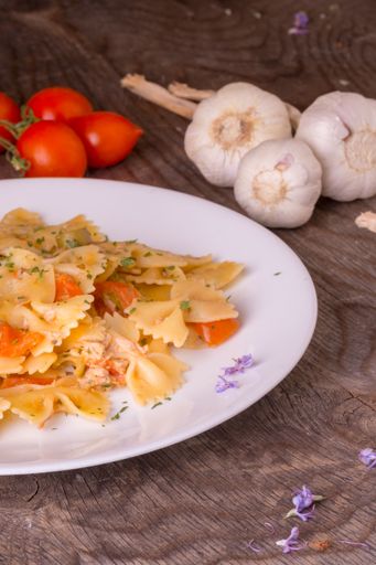 A closeup of a plate of pasta with garlic and tomatoes placed next to it