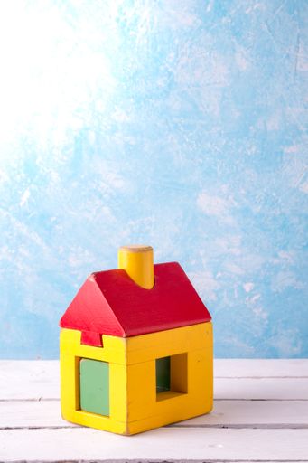 A closeup of a wooden toy house placed on a wooden surface with sky textured wall in the background