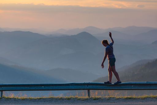 A female walking on a metal street fence carefully with sunset mountains in the background