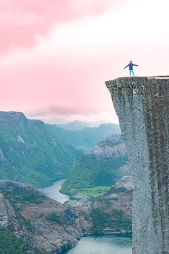 A vertical shot of a person standing on a cliff edge with sunset clouds in the background