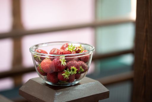 A closeup shot of fresh, delicious strawberries in a transparent glass bowl on a brown wooden surface