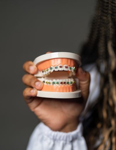 A vertical shot of a person holding prosthesis teeth with braces under the lights
