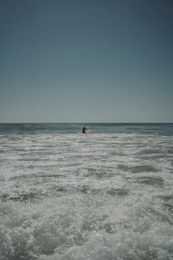 A vertical shot of the ocean with rough waters and a female on a surfboard in the horizom at Cadiz, Andalucia, Spain