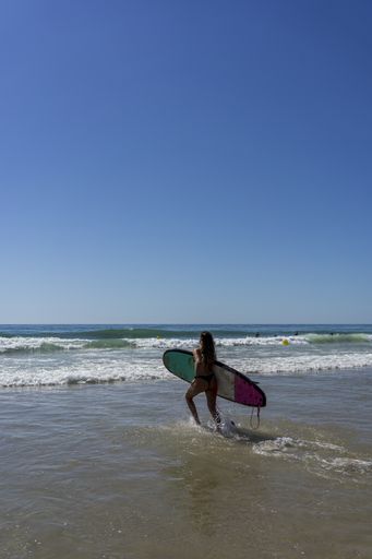A vertical shot of a wavy ocean and a female with a surfing board in Cadiz in Andalucia