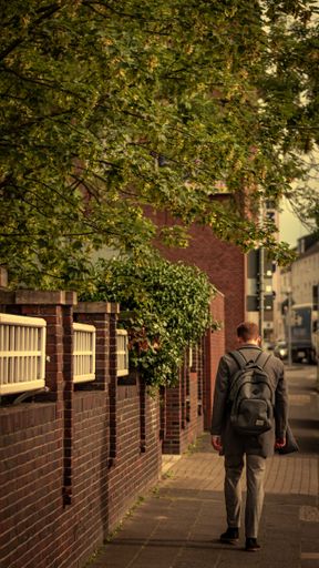 A vertical shot of a man walking alone on the street next to a brick wall in daylight