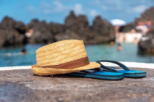 A closeup shot of a sun hat and flipflops on the shore of the coastal town of Porto Moniz, Portugal