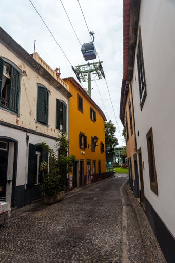 A vertical shot of a cable car going through an alley with houses in Funchal, Madeira, Portugal