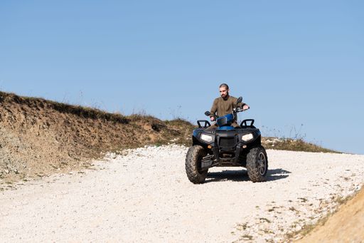 A young man driving a blue off-road quad bike in a rural area in daylight