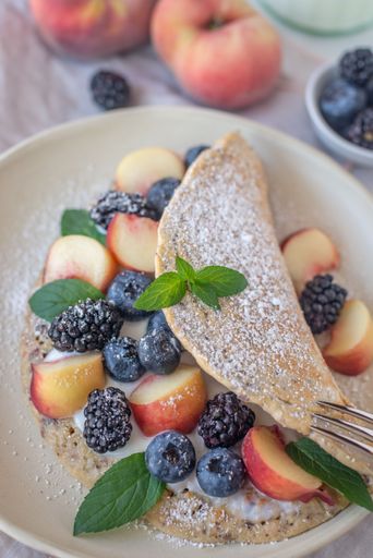 A closeup shot of thin pancakes with berries, fruit, and powdered sugar on a breakfast table