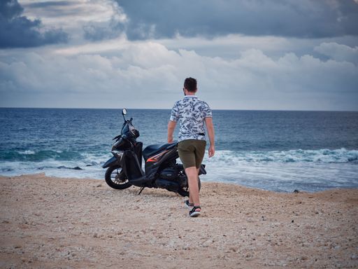A back view of male walking in front of motorcycle in background of sea
