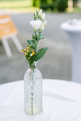 A vertical shot of a clear bottle-vase with flowers as centerpiece on a wedding table