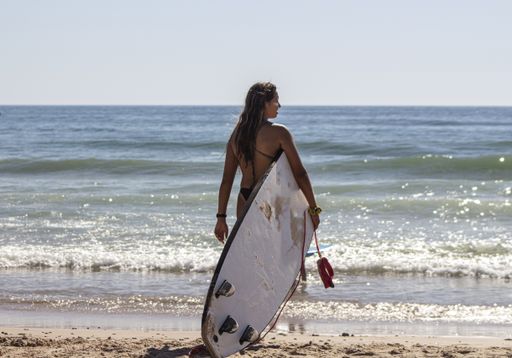 A closeup shot of a beautiful young lady with a surfing board on the beach