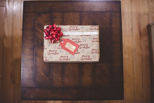 An overhead shot of a Christmas present with a red bow on a wooden table