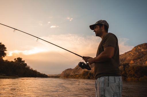 A male fishing in the river with a rod at sunset