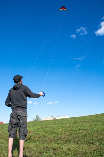A vertical shot of a male holding a kite in the sky