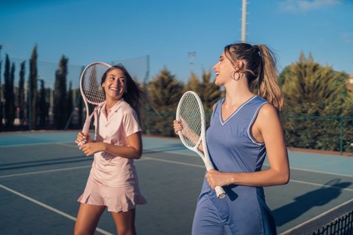 A pair of young female friends with blue and pink athleisure and matching tennis rackets on a court