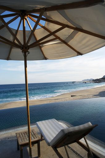 A vertical shot of a trestle and umbrella next to the infinity pool on the sandy beach of Caribbean sea