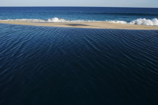 An infinity pool merging to the sandy beach with a blue sea on the opposite side, the Mexican Caribbean