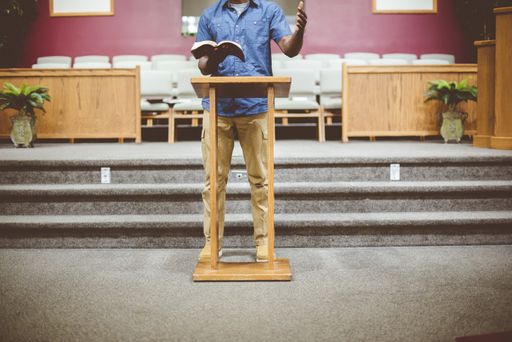 A male standing while reading the bible near a wooden stand with a blurred background