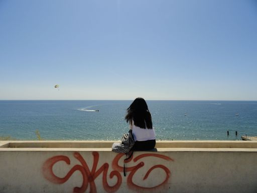 A woman from behind sitting on the stone and enjoying the seascape view