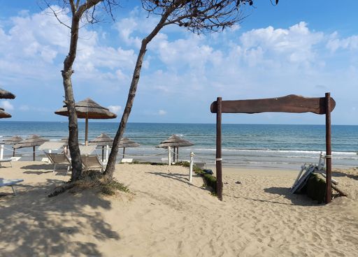 A wooden gate on the beach leading to the sea with deck chairs and umbrellas under blue cloudy sky