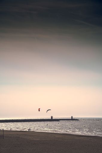 A vertical shot of people walking on the beach and paragliding over sea in the background at sunset