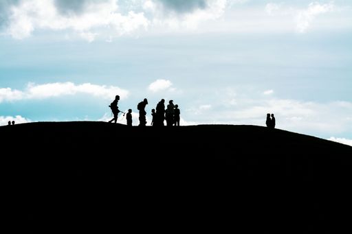 The silhouettes of a group of people walking on a hill under a cloudy sky