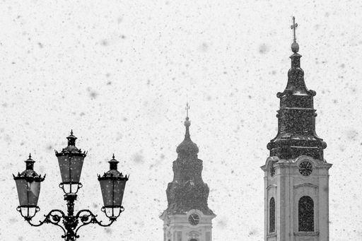 A grayscale shot of two churches towers with cross and street lamps under gray sky