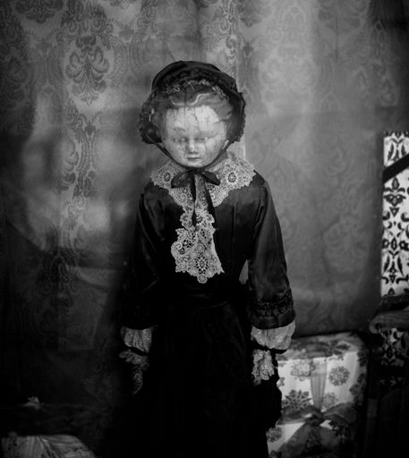 A grayscale of a vintage doll in front of a wall with an ornamental pattern