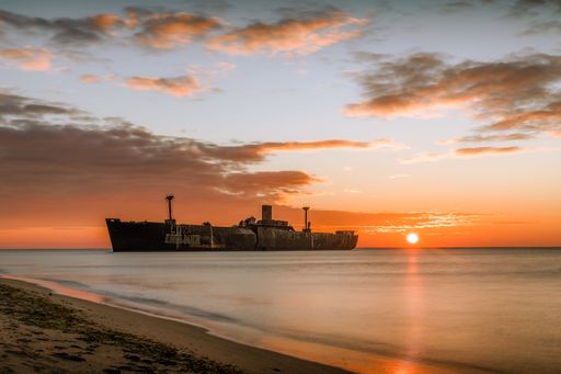 A ship flowing on the sea with a sunset reflection, purple clouds and sky in the background