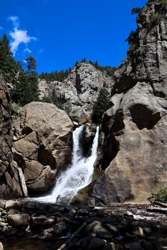 A vertical shot of a waterfall flowing down the rocky mountain slope on a sunny day