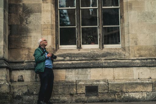 An old man holding a camera and looking up in front of a vintage building