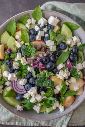 A vertical view of a salad with fruits and vegetables consisting of peach, blueberry, and feta cheese