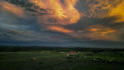 An aerial shot of a green field with houses under a beautiful cloudy sunset sky in Colorado.