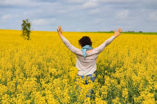 A female opening her hands as a sign of freedom in a yellow field under the cloudy sky