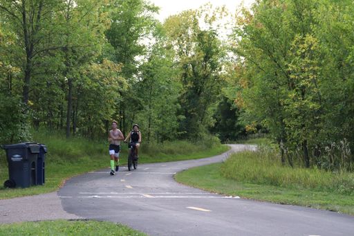 A man running and a woman cycling on a trail in the woods
