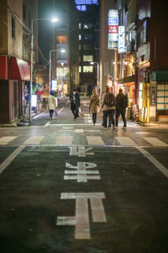 A vertical shot of a narrow Tokyo street at night with people walking