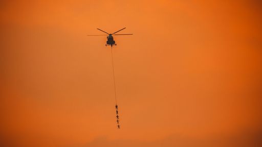 A silhouette of people hanging from a helicopter on a rope in the air
