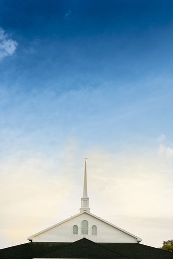 A vertical shot of a church with a blue cloudy sky in the background