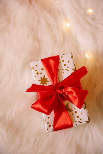 A top view of a Christmas gift box with a red bow on the soft cloth decorated with lights