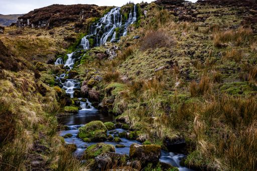 A beautiful waterfall flowing down the rocks covered in moss with mountains in the distance