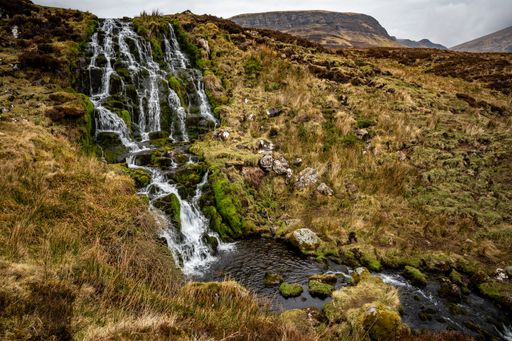 A beautiful waterfall flowing down the rocks covered in moss with mountains in the background
