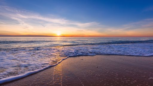 The sea waves splash over the shore at sunset with an orange cloudy sky in the background