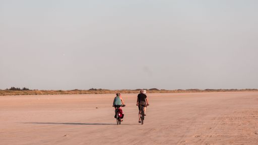 Two women riding bicycles on the sandy shore of Fano Island on a sunny day. Denmark