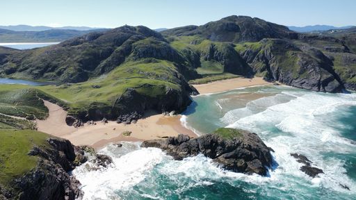 A drone view of Boyeeghter Strand in Rosguill peninsula with green cliffs and ocean waves crashing on the shore
